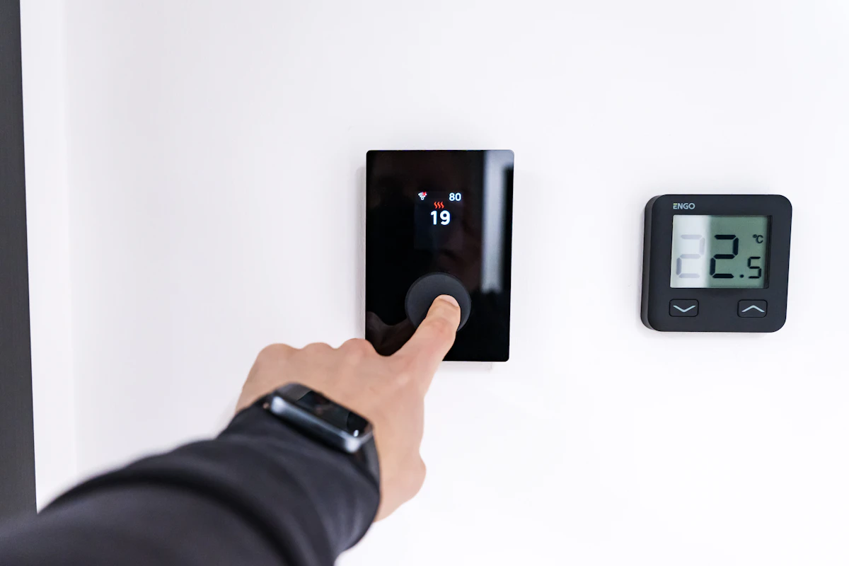 A finger adjusting a digital thermostat on a wall